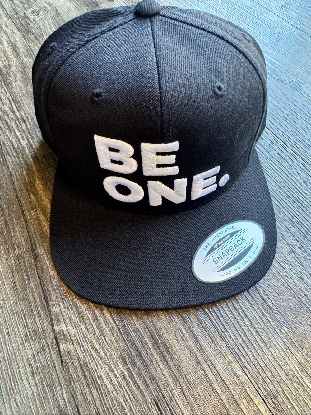 The Classic Black Snapback Hat with White "BE ONE." Embroidery